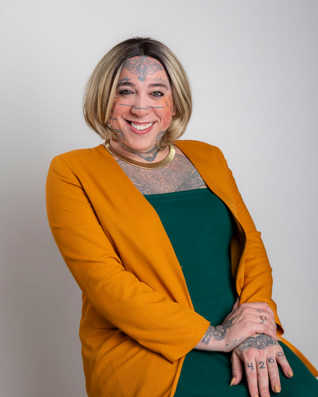 Atena de cardigã amarelo e vestido verde, rindo, em retrato de estúdio.